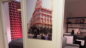 Habitación de hotel con un cartel grande de un edificio histórico, un sofá gris, una mesita con una tetera y suelo de madera.