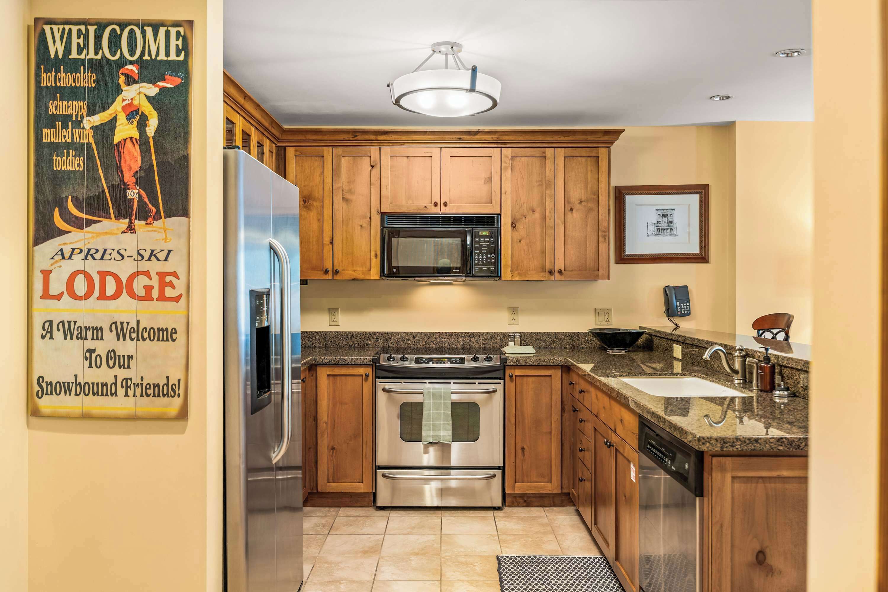 A kitchen with wooden cabinets, stainless steel appliances, a granite countertop, and a ceiling light fixture.