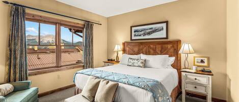 A bedroom with a large bed, two bedside tables, a bench, a chair, and a window with curtains.
