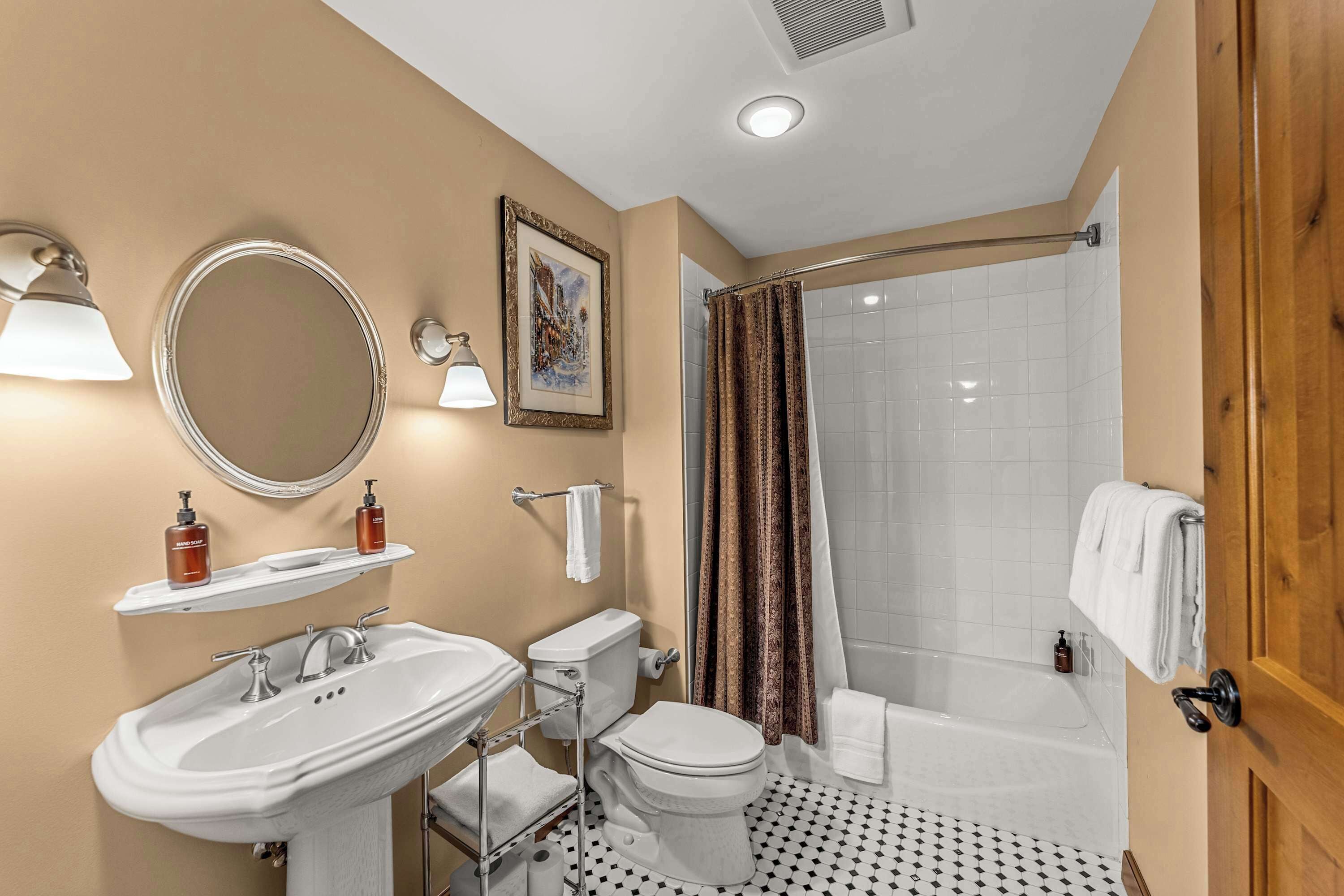 A bathroom with a sink, toilet, and shower. There are two bottles of soap on a shelf above the sink.