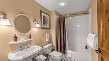 A bathroom with a sink, toilet, and shower. There are two bottles of soap on a shelf above the sink.
