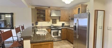 A kitchen with wooden cabinets, a stainless steel refrigerator, a stove, and a sink.