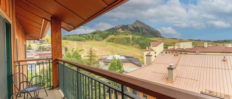 A balcony with a view of a mountain, a chair, and a building with a sloped roof.