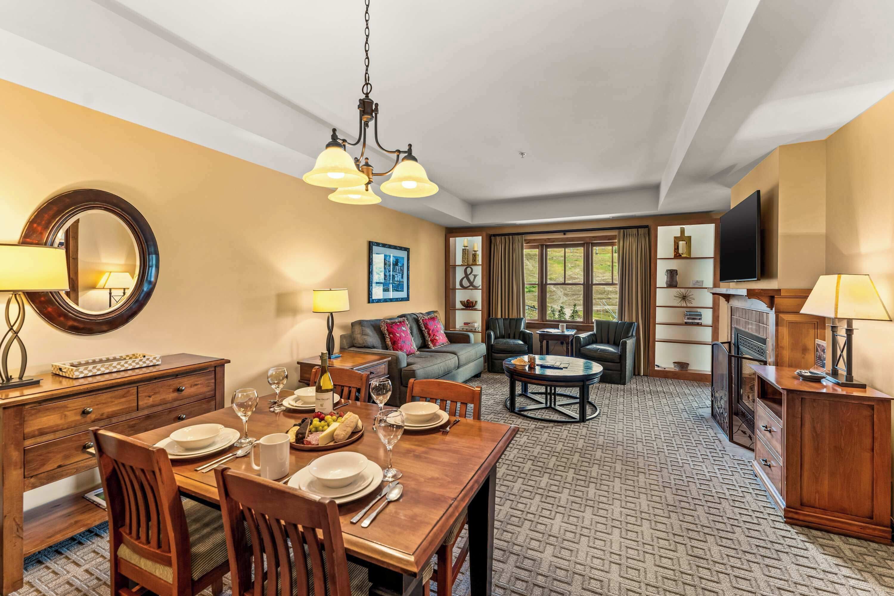 A dining area with a wooden table set for four, a sofa, and a television in the background.