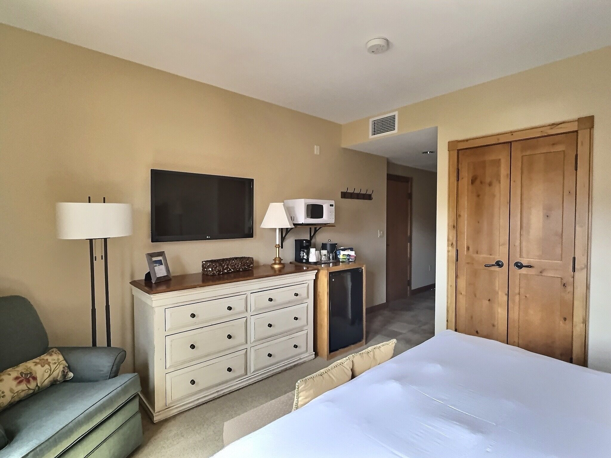 Une chambre d’hôtel comprenant un lit, une commode, un bureau avec une lampe, une télévision, un four à micro-ondes et une porte.
