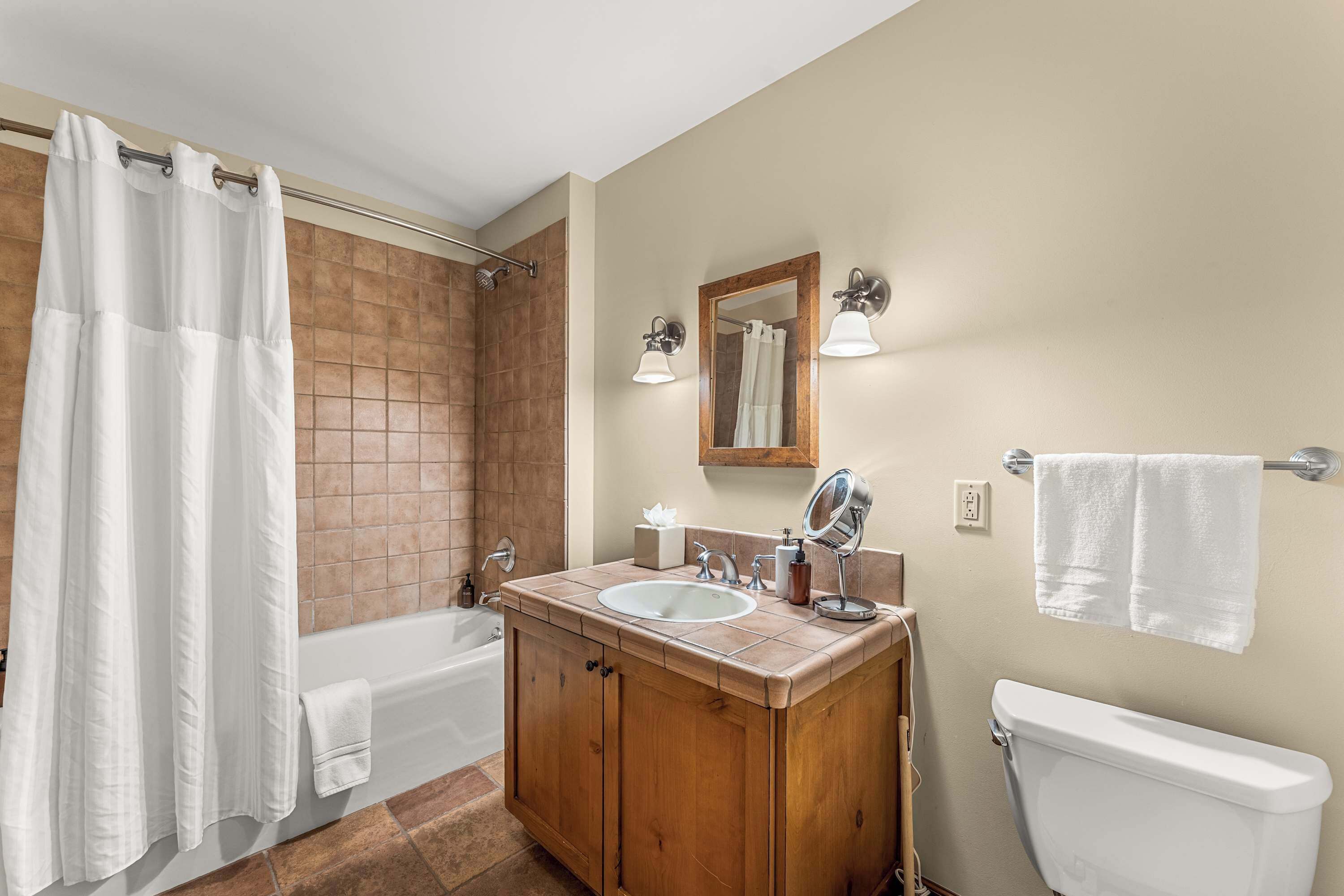 A bathroom with a bathtub, a sink, a toilet, a wooden vanity, a mirror, and a shower curtain.