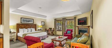 A hotel room with a bed, a dining table set with plates and wine glasses, a TV, and a fireplace.