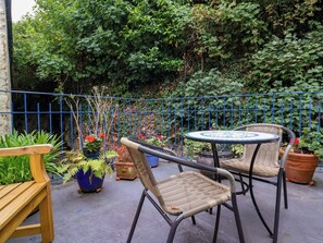 An outdoor seating area with wicker chairs and a round table, surrounded by potted plants and a blue metal fence. - Baywatch (Lynton)