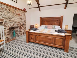Una cama de madera con cabecera, una chimenea de piedra y una alfombra estampada.