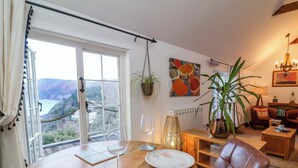 Ein Essbereich mit Tisch für zwei Personen, Blick ins Freie und eine gemütliche Sitzecke mit Sessel und Lampe.