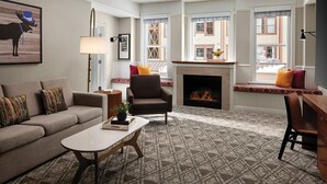 Una sala de estar con sofá, sillón, chimenea y ventanas amplias.
