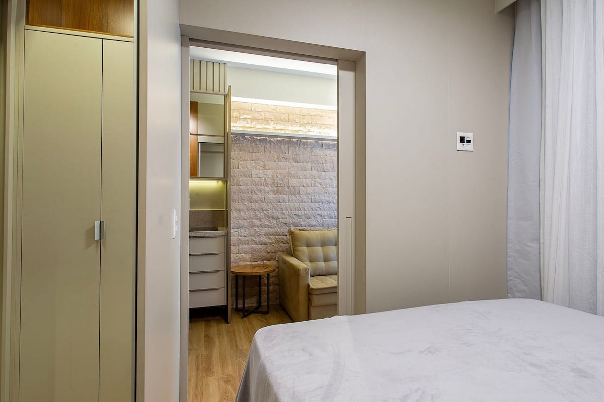 Une chambre à coucher comprenant un lit, une armoire, un coin salon avec un fauteuil et un mur en pierre.