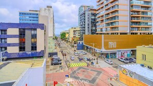 A city street with modern buildings, a prominent yellow building with 'NAU' signage, and a pedestrian crossing. - Convenience and Comfort 90m From Farol da Barra Beach - Hbas (Salvador)