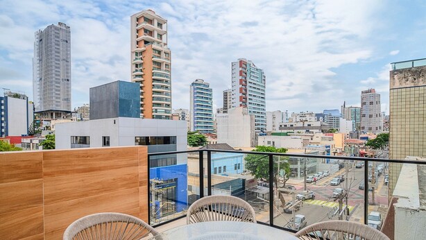 A cityscape view from a balcony with modern buildings, a clear sky, and a street below. - Convenience and Comfort 90m From Farol da Barra Beach - Hbas (Salvador)