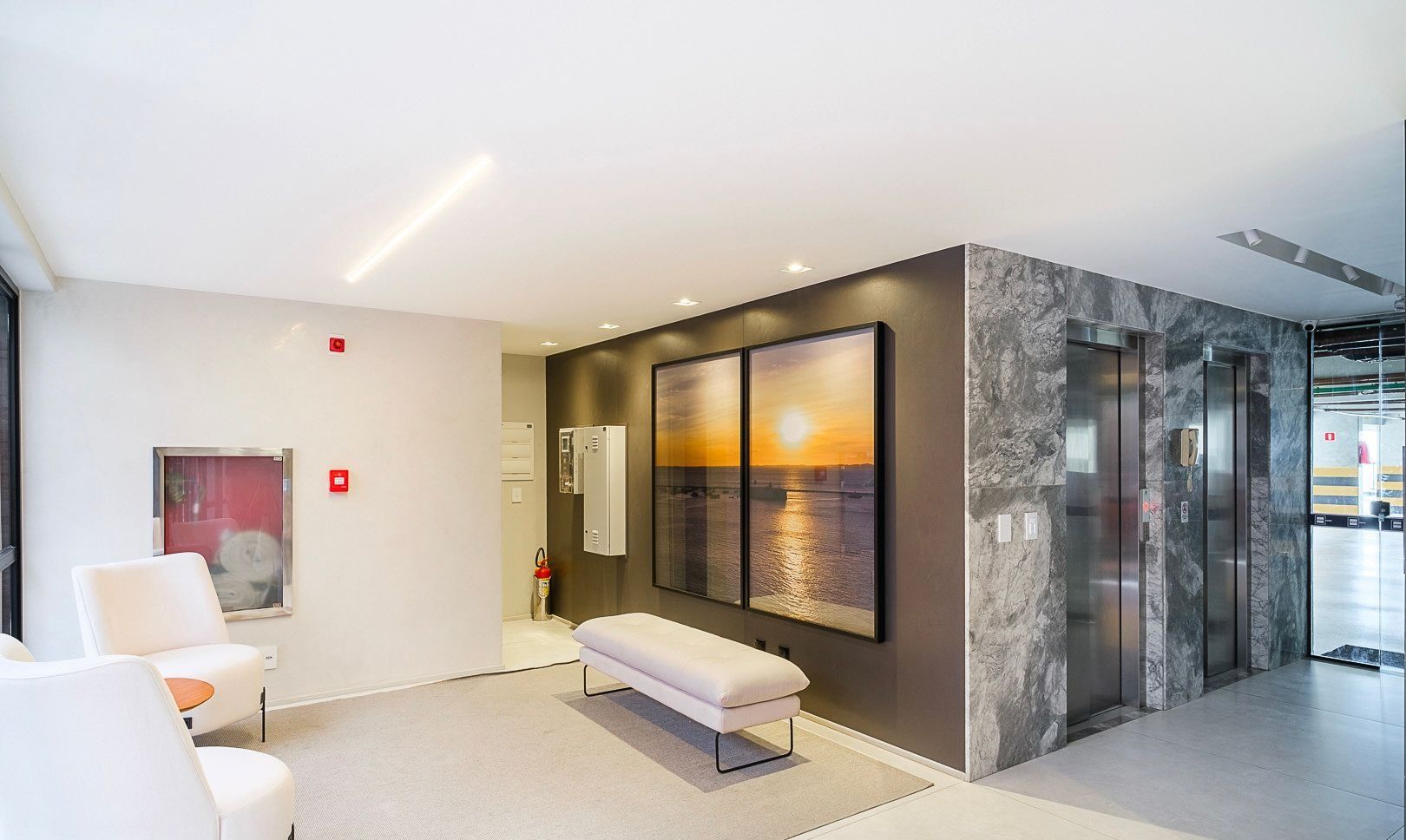 Um lobby moderno com um banco, área de estar e uma grande obra de arte na parede retratando um pôr do sol sobre a água.