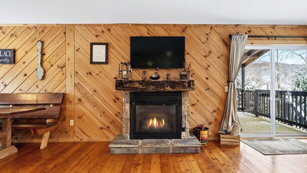 Ein gemütliches Wohnzimmer mit Kamin aus Stein, Holzwänden, einem Flachbildfernseher und einer hölzernen Bank.