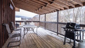 Eine überdachte Holzterrasse mit Grill und Sitzgelegenheit, mit Blick auf eine verschneite Landschaft.