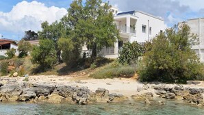A coastal building with a balcony, surrounded by trees and rocky terrain. - Luxurious beach villa in Apulia (Marina di Pulsano)