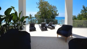 A covered outdoor seating area with lounge chairs and a table, overlooking a scenic view of the sea and trees. - Luxurious beach villa in Apulia (Marina di Pulsano)
