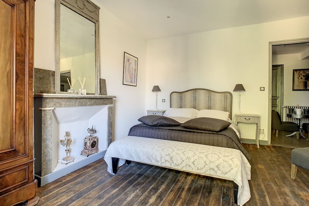 A bedroom with a large bed, a wooden wardrobe, a fireplace, and a mirror.