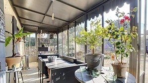 Un patio cubierto con mesas y sillas, plantas en macetas y vistas del paisaje circundante.