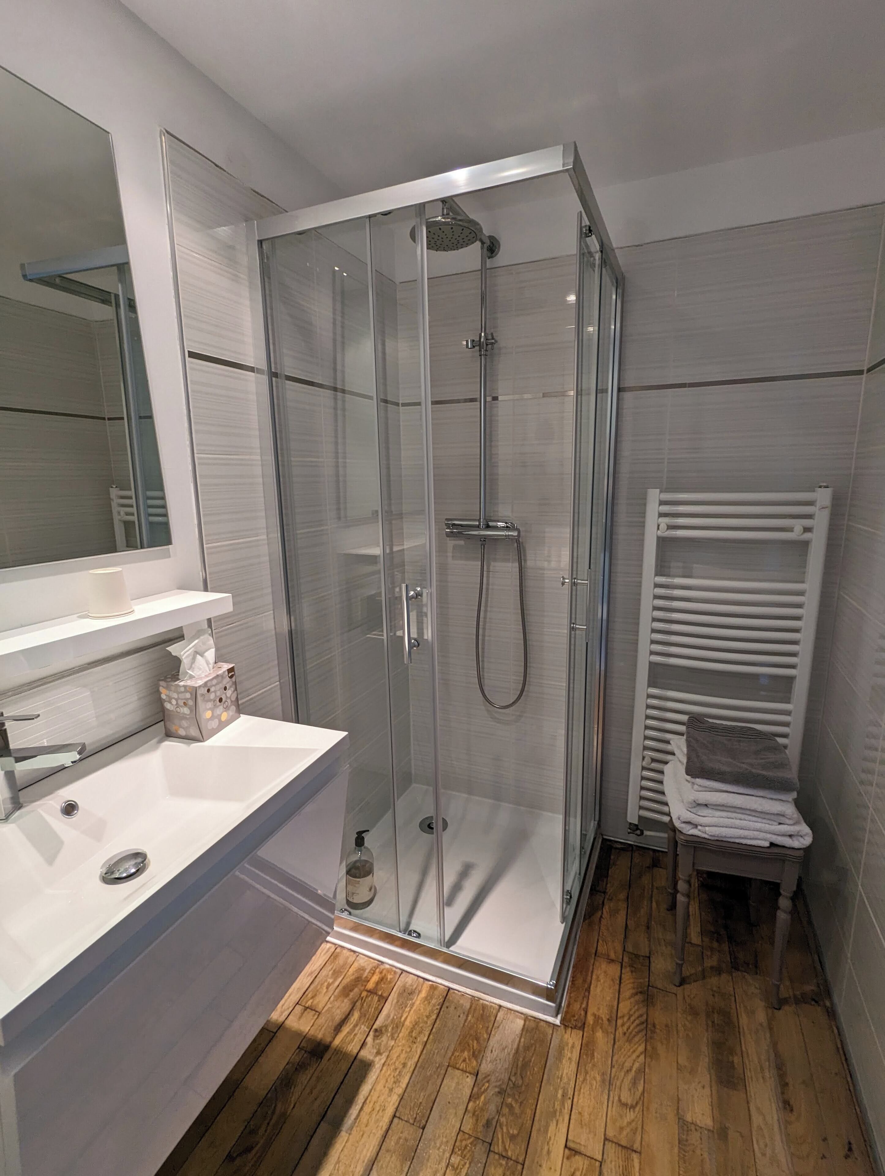 A modern bathroom with a glass-enclosed shower, a white sink, and a towel rack.