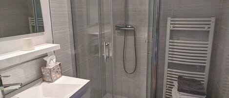 A modern bathroom with a glass-enclosed shower, a white sink, and a towel rack.