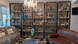 Una sala de estar con piso a cuadros, un sofá, una mesita de centro y un sillón de cuero. Hay un aparador de vidrio con estantes que contienen varios objetos.