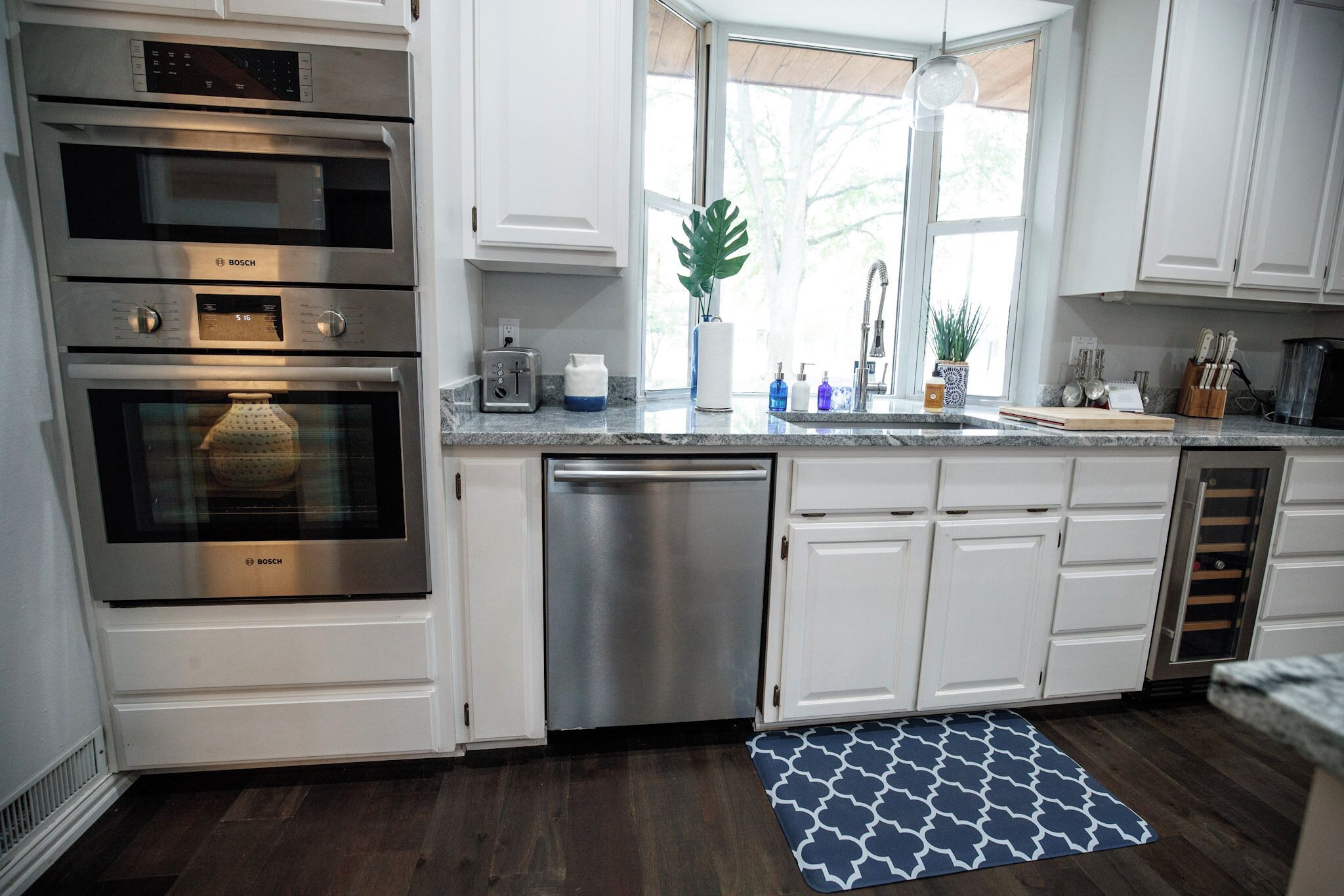 A modern kitchen with white cabinets, stainless steel appliances, a dishwasher, and a window with a view of trees.