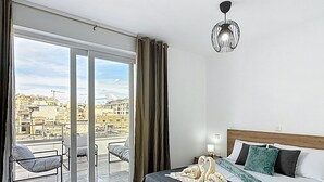 A hotel room with a bed, a balcony with chairs, and a city view. - Luxury Penthouse Holiday Stay Property in Gzira (Il-Gżira)