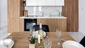 A modern kitchen with wooden cabinets, a white countertop, and a dining table set for four. - Luxury Penthouse Holiday Stay Property in Gzira (Il-Gżira)
