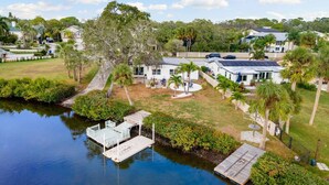 A waterfront property with a dock, a grassy yard, and a house with a large deck. - Swan Lake Inn - Waterfront Oasis • Firepit • BBQ (New Port Richey)