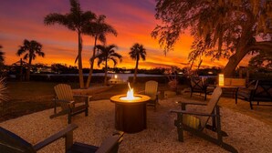 An outdoor seating area with a fire pit, chairs, and tables, overlooking a body of water at sunset. - Swan Lake Inn - Waterfront Oasis • Firepit • BBQ (New Port Richey)