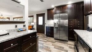 A modern kitchen with dark wood cabinets, stainless steel appliances, granite countertops, and a herringbone wood floor pattern. - Swan Lake Inn - Waterfront Oasis • Firepit • BBQ (New Port Richey)