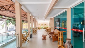 A covered outdoor seating area with wooden furniture and a glass wall on one side. - Hotel Durma Bem (Castanhal)