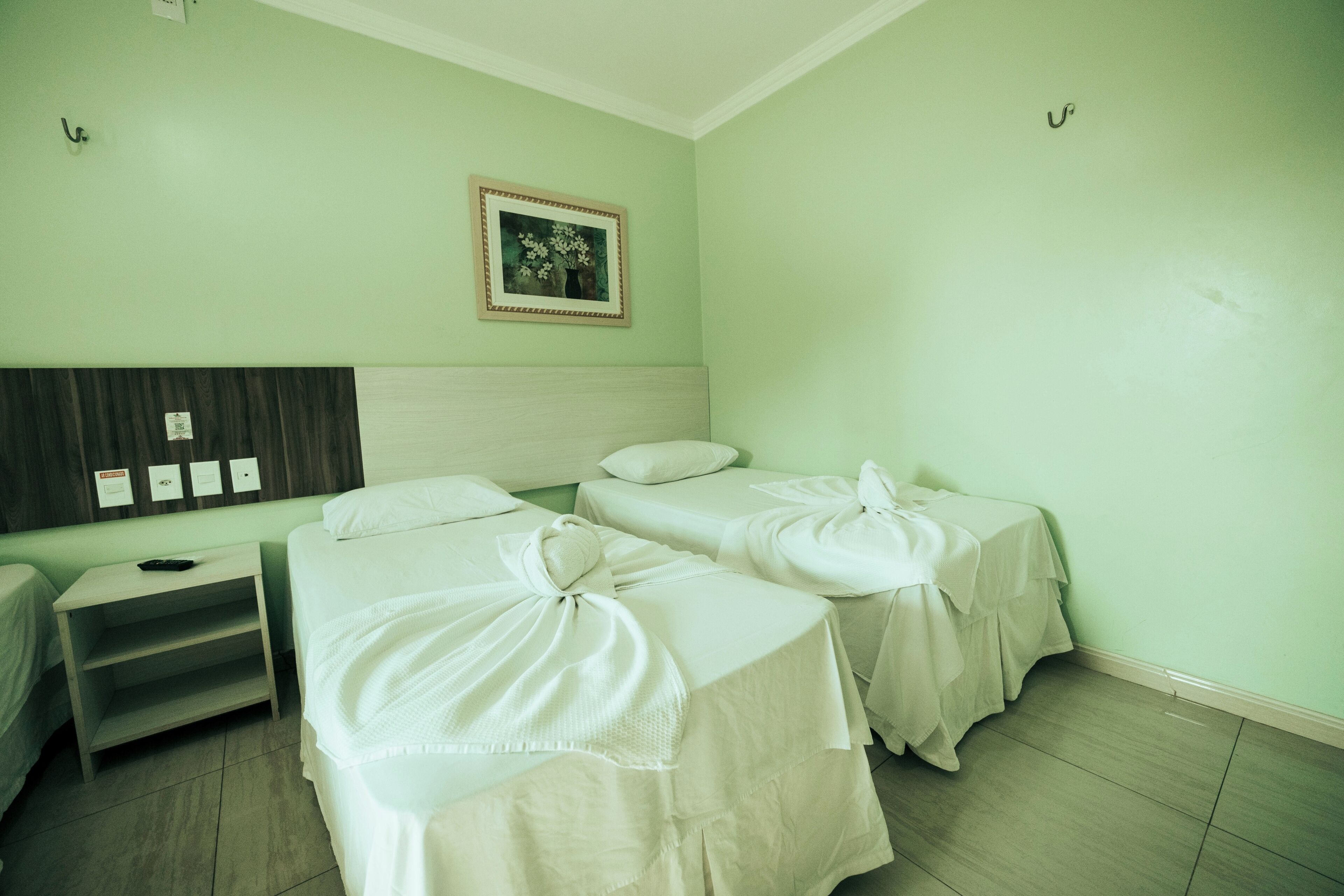 A room with two beds, a nightstand, a wall-mounted picture, and a light switch.