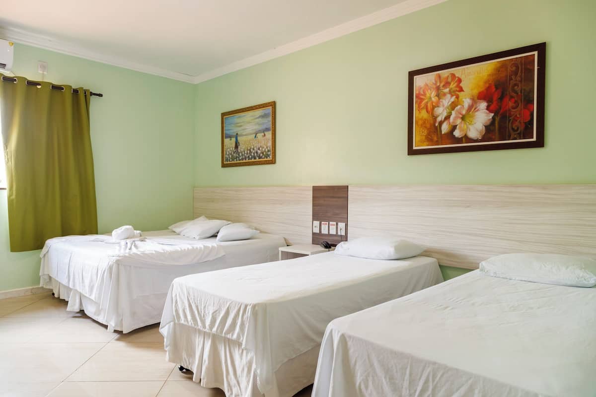 Habitación de hotel con dos camas individuales, cabecera, un cuadro de flores y una cortina verde.
