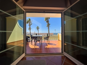 A balcony with a table and chairs, palm trees, and a clear sky. - Garden Park by ACasaDasCasas (Ericeira)