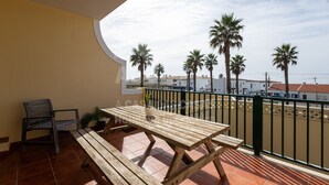 Ein Balkon mit Holztisch und -stühlen, einem Blumentopf und Blick auf Palmen und Gebäude.