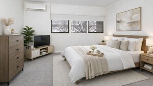 A bedroom with a bed, bedside tables, a TV, a dresser, and a window with a view of trees. - North Adelaide Townhouse (North Adelaide)