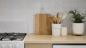 A kitchen with a gas stove, a wooden cutting board, a utensil holder, and a potted plant. - North Adelaide Townhouse (North Adelaide)
