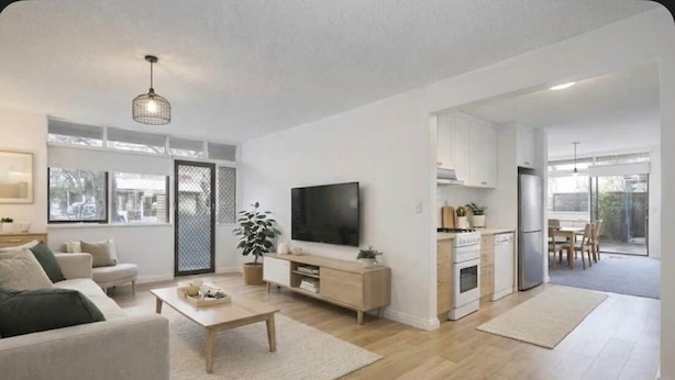 A modern living room with a sofa, coffee table, TV, and a kitchen area with cabinets and appliances. - North Adelaide Townhouse (North Adelaide)