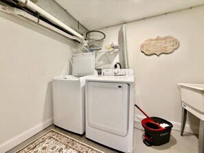 A laundry room with two front-loading washers, a drying rack, a bucket, and a sign indicating the room's purpose.