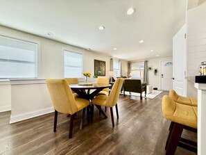 A dining area with a round table and four chairs, a kitchen area with a counter and cabinets, and a door leading to another room.
