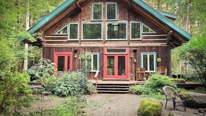 Eine zweistöckige Holzhütte mit einem grünen Dach, umgeben von üppiger Vegetation.
