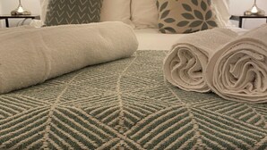 A neatly made bed with a geometric-patterned bedspread, two rolled towels, and two bedside lamps on either side. - Ushaw Hilltop View- Comfortable 2-Bed Home Near Durham University & City (Ushaw Moor)