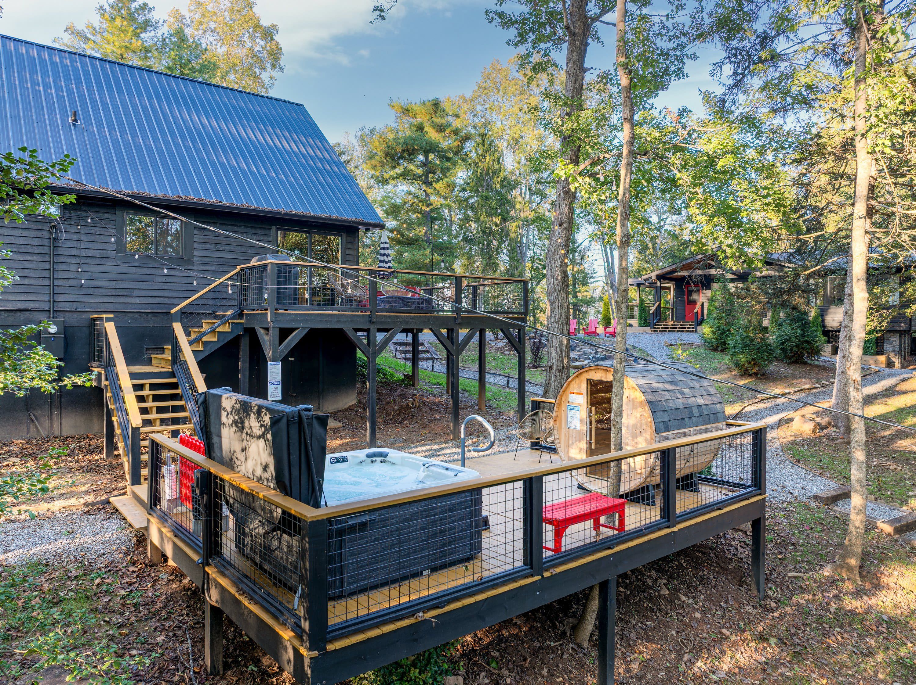 Eine Holzterrasse mit Whirlpool, einer überdachten Sitzecke und einer Treppe, die zu einem Haus mit blauem Dach führt.