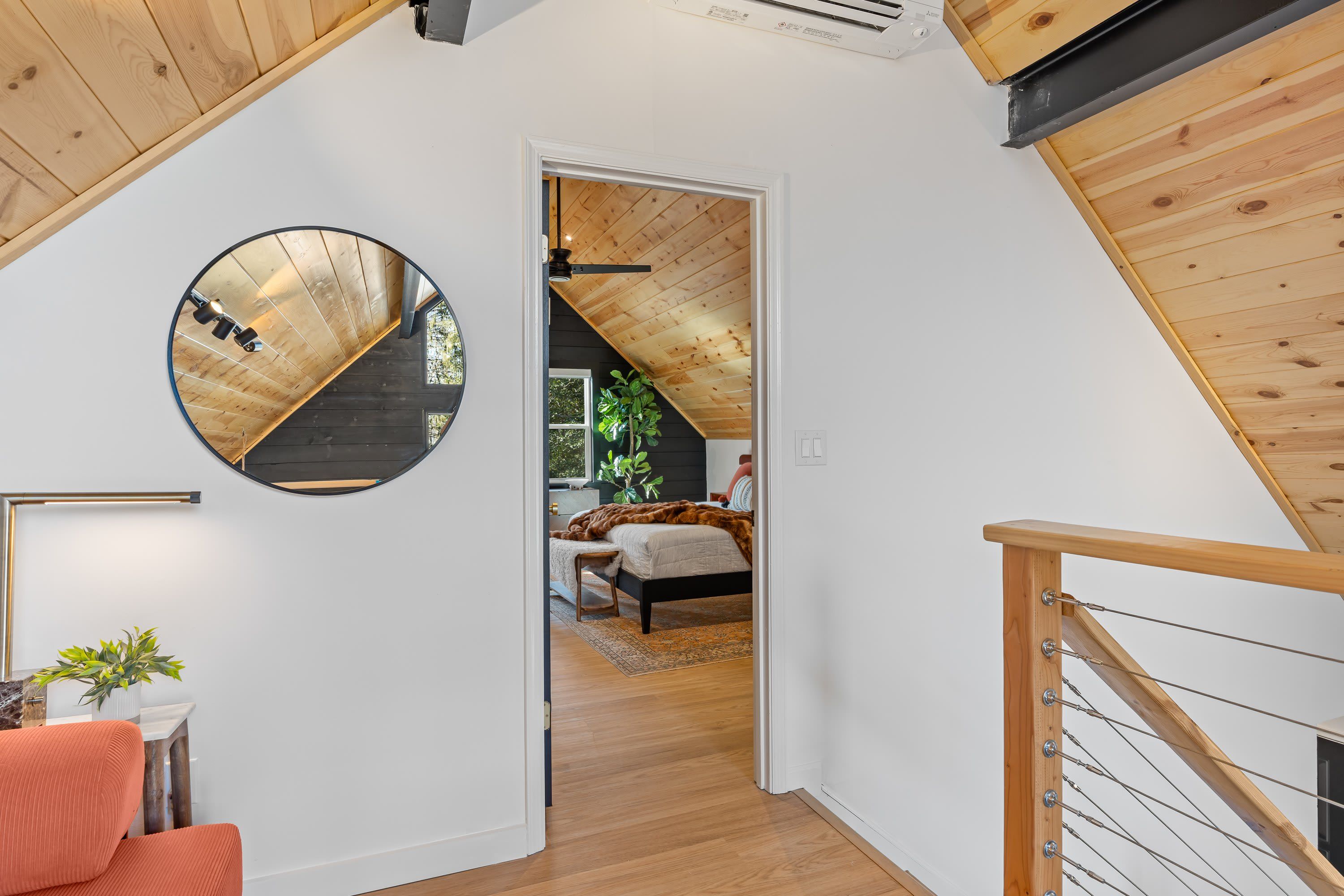 A modern interior with a circular mirror, a staircase, and a view into a bedroom.