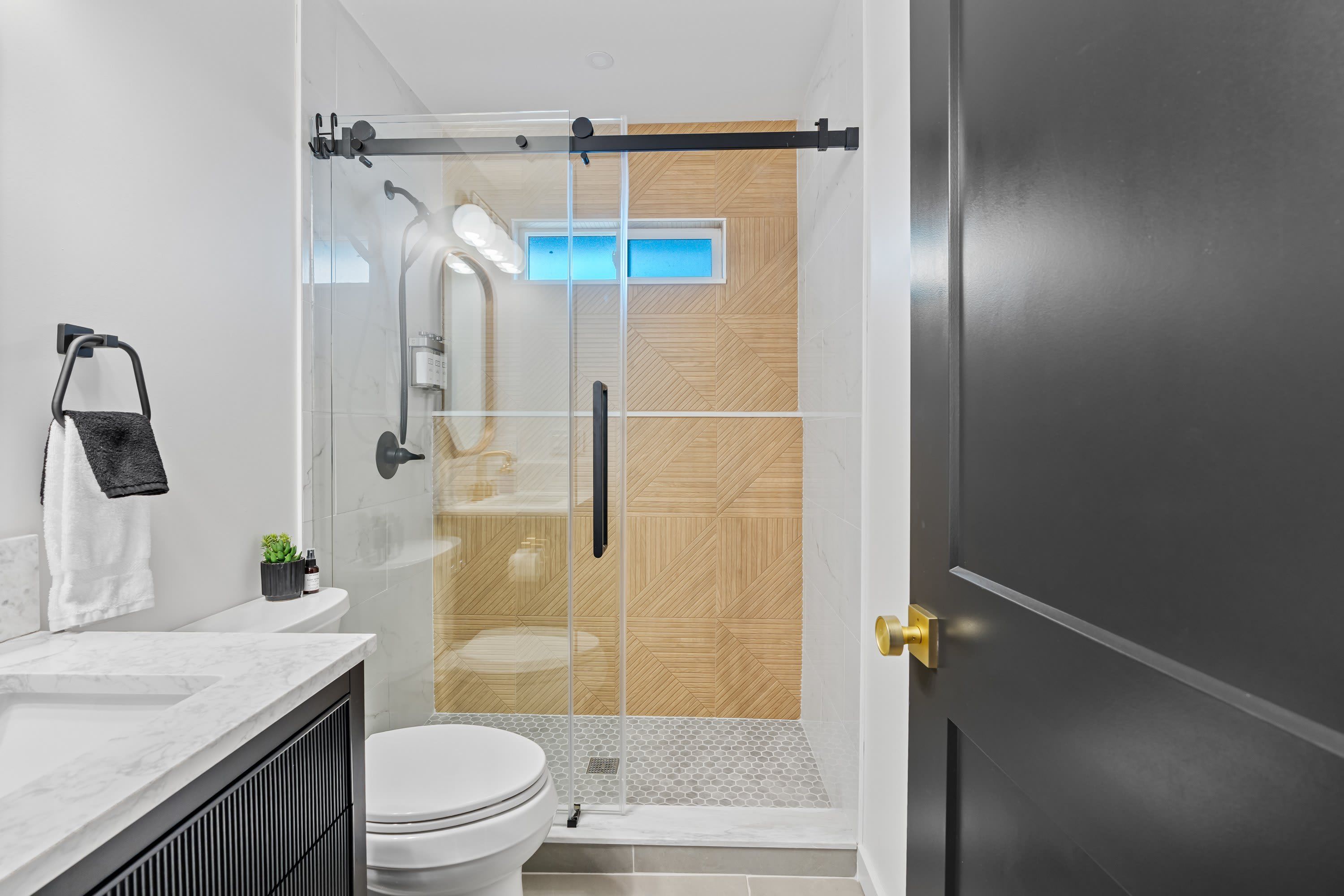 A modern bathroom with a glass shower enclosure, a toilet, and a sink with a marble countertop.