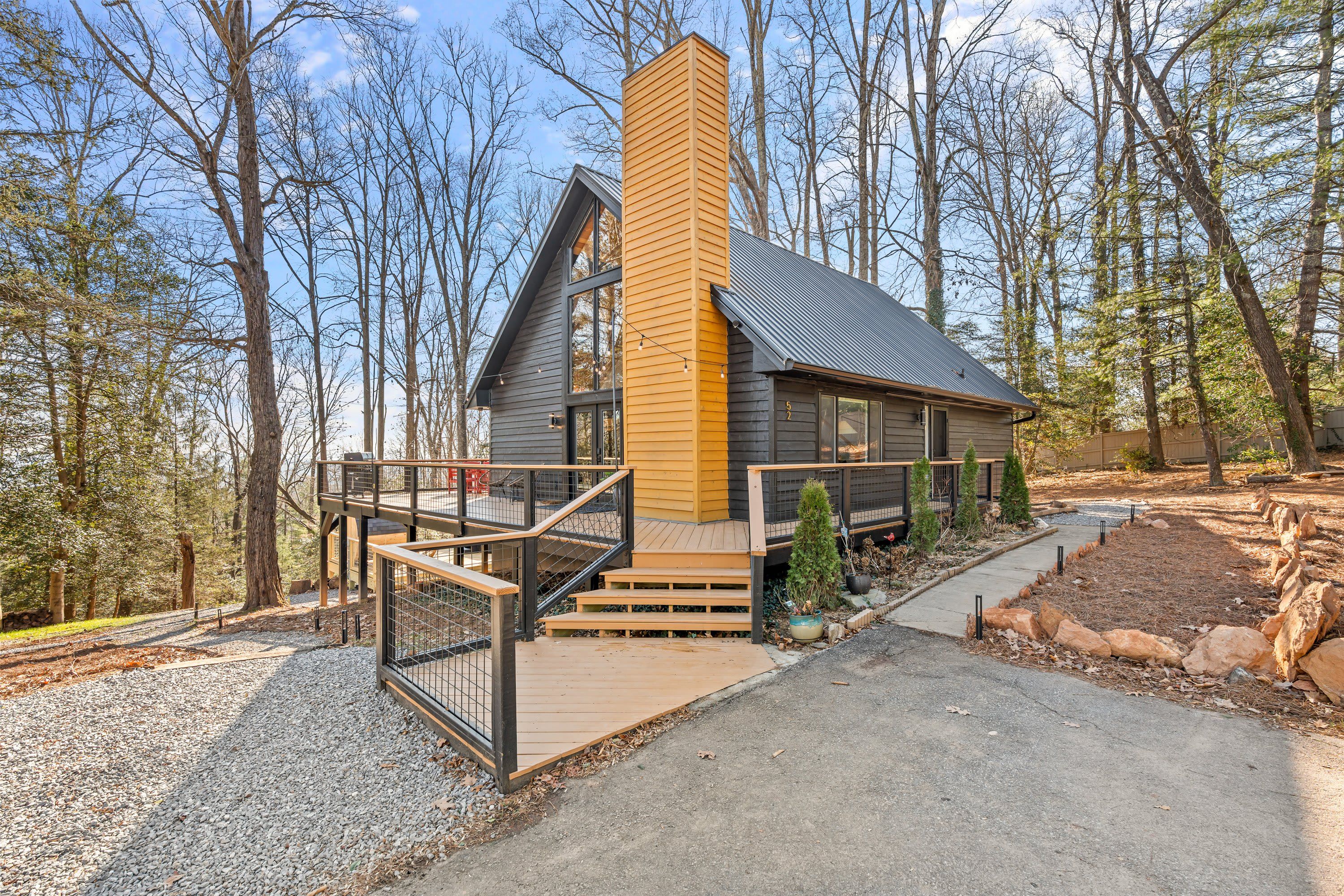 Une cabane moderne dotée d’une cheminée imposante, d’une terrasse avec une balustrade et d’un chemin de pierre menant à l’entrée.